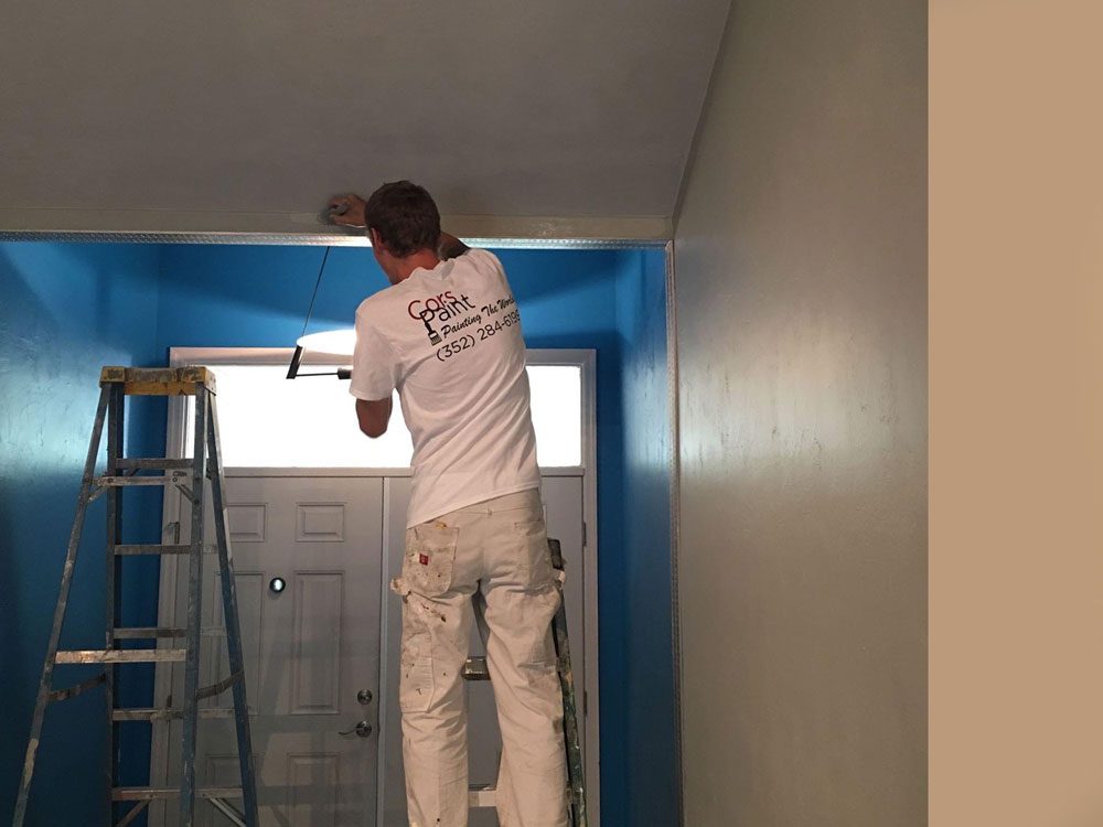 man painting the side of a house while standing on a ladder